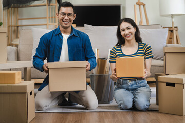 Young couple relaxing sitting on the floor around cardboard boxes at home, smiling happy moving to a new house.