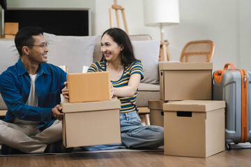 Young couple relaxing sitting on the floor around cardboard boxes at home, smiling happy moving to a new house.