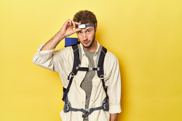 Traveler with mountain backpack, mat, and headlamp on yellow backdrop