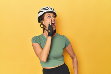 Cyclist middle aged woman with helmet and gloves posed shouting and holding palm near opened mouth.