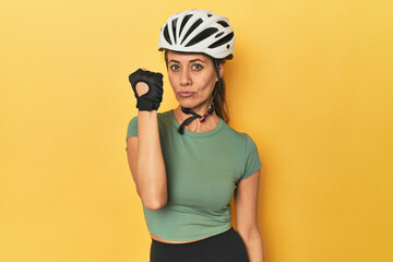 Cyclist middle aged woman with helmet and gloves posed showing fist to camera, aggressive facial expression.