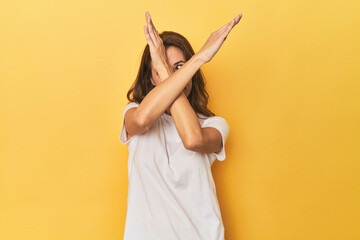 Middle-aged caucasian woman on yellow keeping two arms crossed, denial concept.