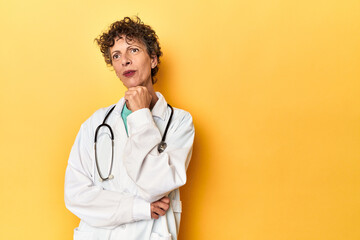 Caucasian mid-age female doctor on yellow studio looking sideways with doubtful and skeptical expression. - obrazy, fototapety, plakaty
