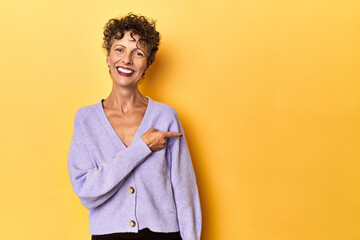 Mid-aged caucasian woman on vibrant yellow smiling and pointing aside, showing something at blank...