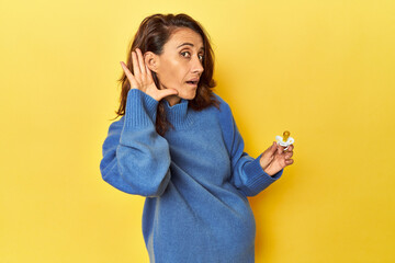 Pregnant woman with pacifier on yellow studio trying to listening a gossip.