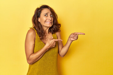 Middle-aged woman on a yellow backdrop shocked pointing with index fingers to a copy space.