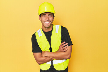 Latino worker in yellow vest and helmet laughing and having fun.