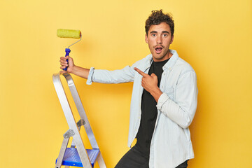 Man with ladder and paint roller on yellow pointing to the side