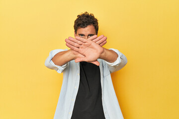 Young Latino man posing on yellow background doing a denial gesture