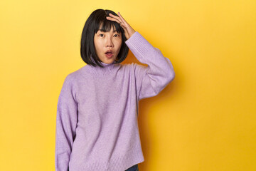 Young Chinese lady, yellow studio background shouts loud, keeps eyes opened and hands tense.