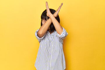 Young Chinese lady, yellow studio background keeping two arms crossed, denial concept.