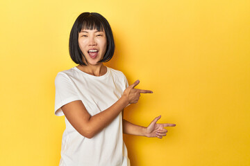 Young Chinese lady, yellow studio background pointing with forefingers to a copy space, expressing...