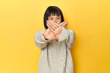 Young Chinese lady, yellow studio background doing a denial gesture