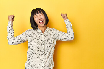 Young Chinese lady, yellow studio background raising fist after a victory, winner concept.