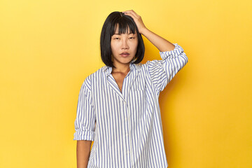 Young Chinese lady, yellow studio background tired and very sleepy keeping hand on head.