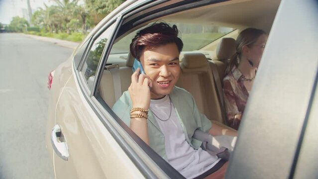 Side view of young Asian man calling on mobile phone while sitting in taxi next to his Caucasian girlfriend
