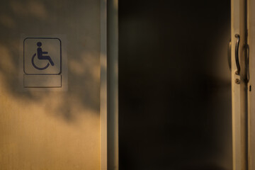 Handicapped or wheelchair symbol shown on exterior old white of the public toilet wall with orange...