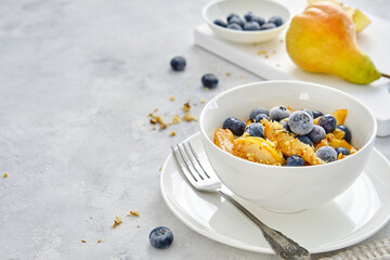 Cottage cheese with pieces of pears, nuts and blueberries in a white cup on a light-gray background. Delicious and healthy breakfast
