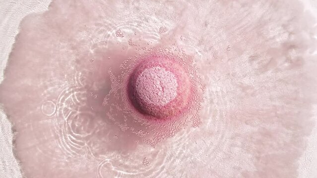 Pink bath bomb ball dissolves in water with white foam bubbles. Cosmetic product natural and skin care. Clear water with reflections sunlight and shadows. . High quality 4k footage
