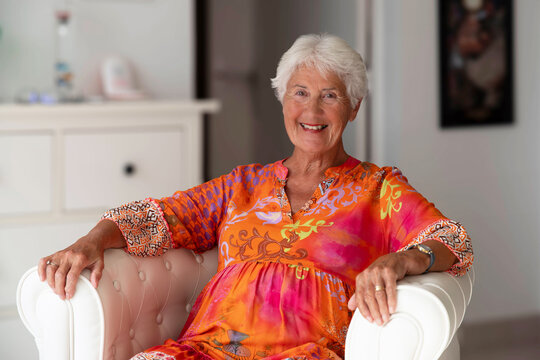 A happy, smiling elderly woman sitting in an armchair at home