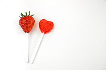 2 Erdbeer-Lollies, eine echte Erdbeere auf einem Lollistiel und ein herzförmiger roter Lolli, weißer Hintergrund, horizontal, freier Raum