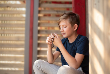 An 11 year old Catholic boy reads the rosary prayer, holds a wooden rosary with 10 beads in his...