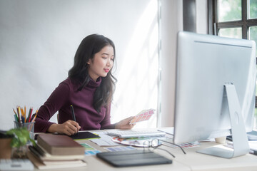 Graphic designer freelance women choosing color on color swatch sample to sketching logo brand on digital tablet while working designing about graphic design with technology equipment in home studio