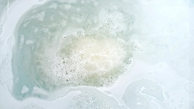 Bath bomb ball in the shape of a heart dissolves in water with white foam bubbles. Cosmetic product natural and skin care. Clear water with reflections sunlight and shadows. . High quality 4k footage
