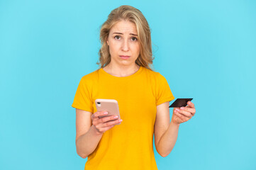 Sad woman looking at camera, holding smartphone and plastic card in hands