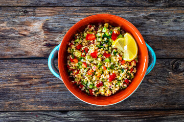 Tabbouleh salad - bulgur groats, tomatoes, cucumber, parsley, lemon, onion and fresh mint leaves on wooden background
