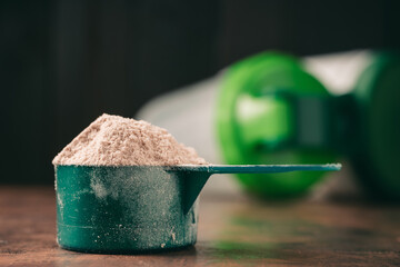 Chocolate whey protein powder in measuring spoon and shaker on dark background. healthy eating, bodybuilding food supplements