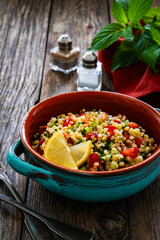 Tabbouleh salad - bulgur groats, tomatoes, cucumber, parsley, lemon, onion and fresh mint leaves on wooden background
