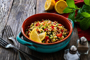 Tabbouleh salad - bulgur groats, tomatoes, cucumber, parsley, lemon, onion and fresh mint leaves on wooden background
