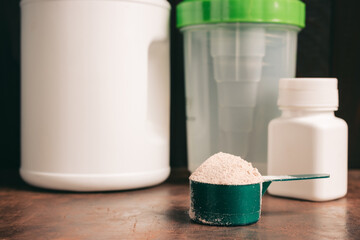 Chocolate whey protein powder in measuring spoon, old rusty dumbbell, shaker, plastic bottle on dark background. healthy eating, bodybuilding food supplements
