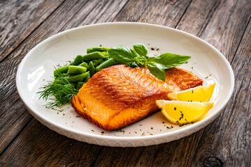 Seared salmon steak with green bean and lemons on wooden table
