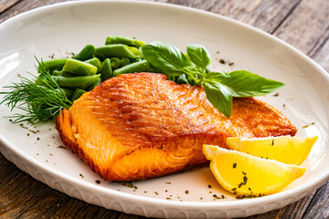 Seared salmon steak with green bean and lemons on wooden table
