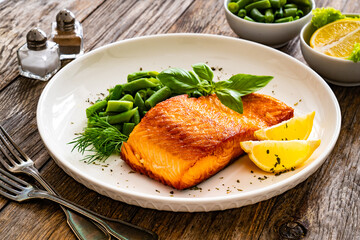 Seared salmon steak with green bean and lemons on wooden table
