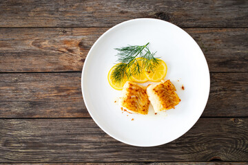Seared cod loin and sliced lemon on wooden table
 - obrazy, fototapety, plakaty