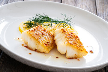 Seared cod loin and sliced lemon on wooden table
