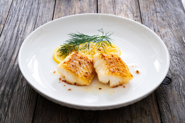 Seared cod loin and sliced lemon on wooden table
