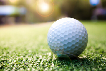 Golf ball placed on grass, background with bokeh and flare.