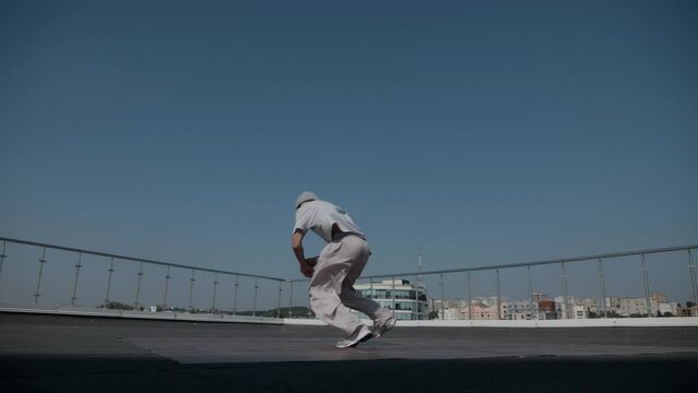 The guy coolly dances breakdance on the roof of the house. A man dances an energetic athletic dance.