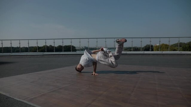 The guy coolly dances breakdance on the roof of the house. A man dances an energetic athletic dance.	
