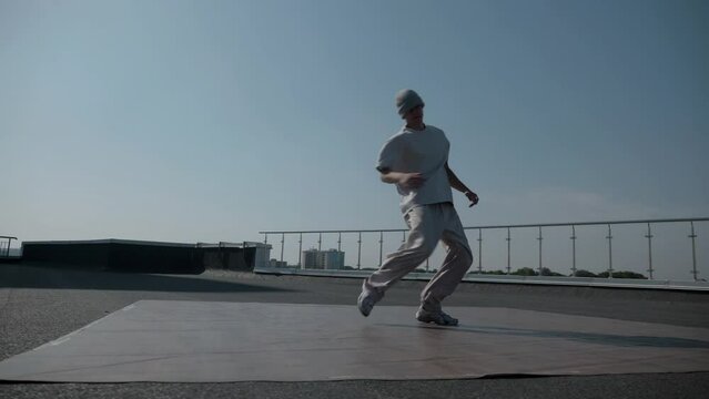 The guy coolly dances breakdance on the roof of the house. A man dances an energetic athletic dance.	
