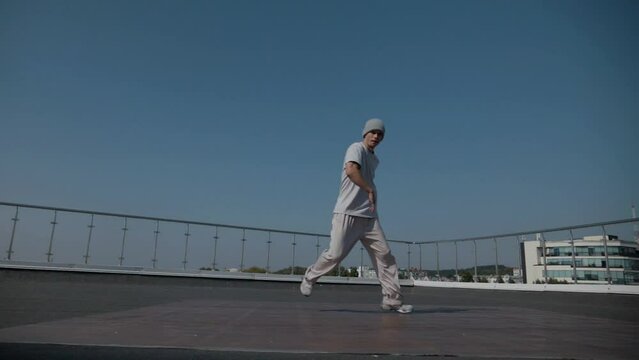 The guy coolly dances breakdance on the roof of the house. A man dances an energetic athletic dance.	
