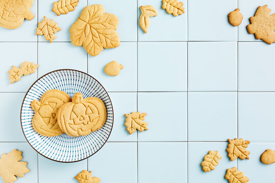 Freshly baked homemade pumpkin cookies for Halloween in a plate with a blue pattern on a tile background.