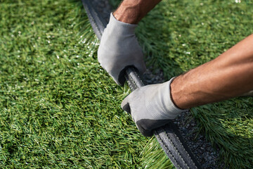Hands rolling a green imitation grass. The material is for carpet, flooring, wall and sports stadiums. Landscaping of the yard with artificial turf. Gardener hands hold a roll of artificial grass. - obrazy, fototapety, plakaty