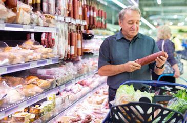 Elderly man chooses sausage in supermarket