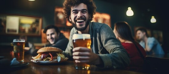 Joyful young man enjoying burgers and beer with friends at a pub With copyspace for text
