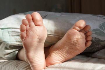 Feet under a light blanket on the bed